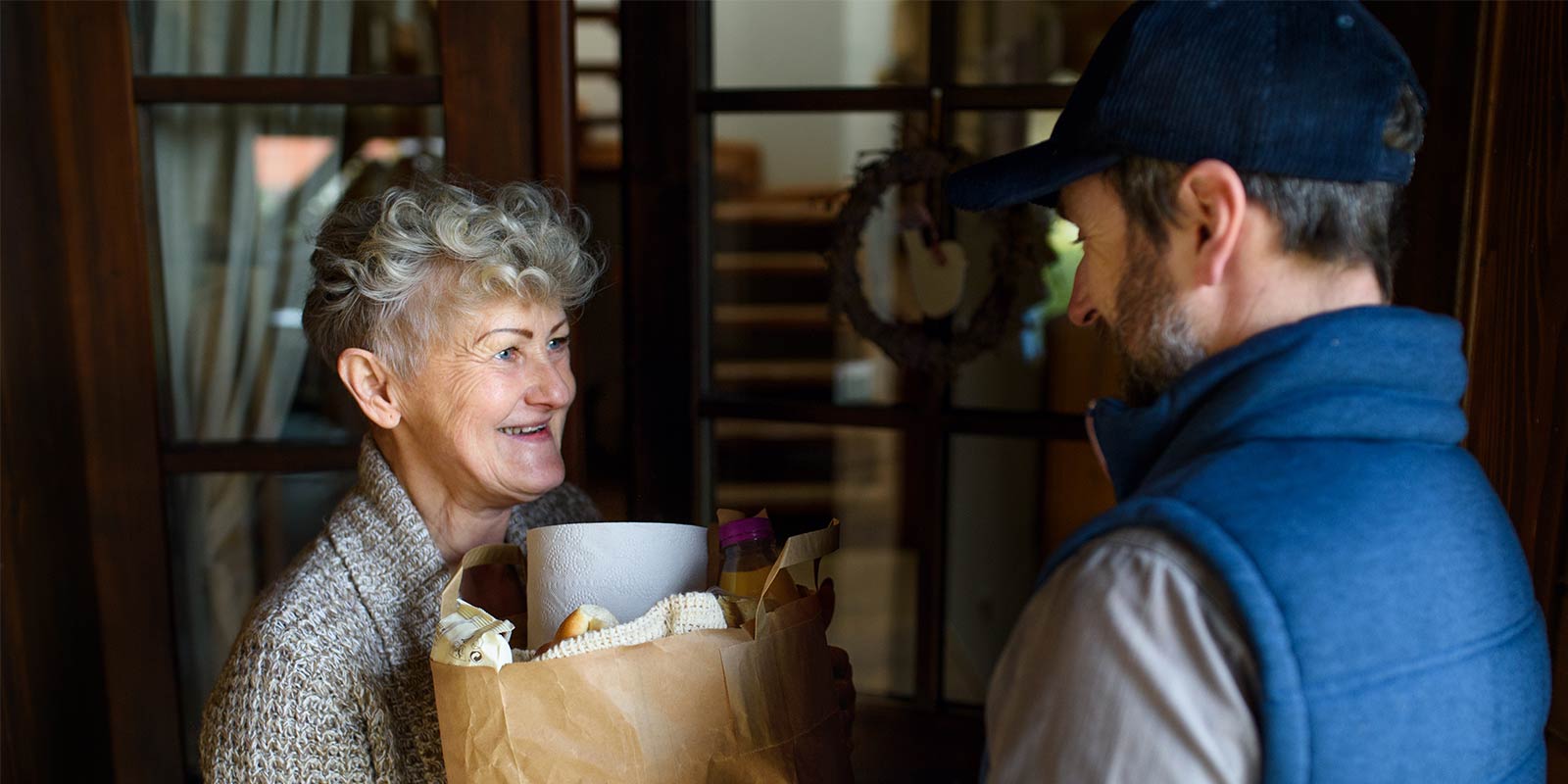 A delivery worker hands a packaged meal to an older adult at their front door