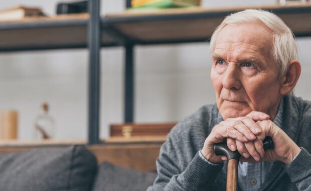 Northern Virginia retired man with grey hair holding walking cane in living room