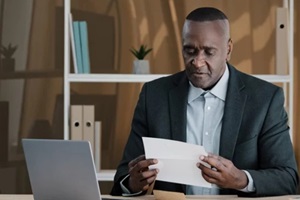 Northern Virginia old man senior mature male in office opening paper envelope reading letter with good news