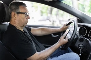 senior in his 70s driving a car and using his mobile phone