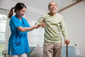 young carer supporting helping senior man stand up with walking stick from sofa