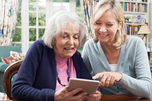 female neighbor showing senior woman how to use digital tablet
