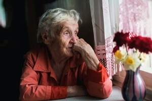 elderly woman looks sadly out the window