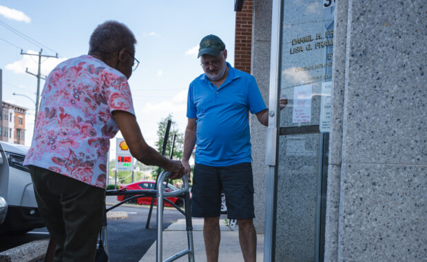 scnova volunteer wolf opens the door for his participant passenger as she enters the doctor's office using a walker